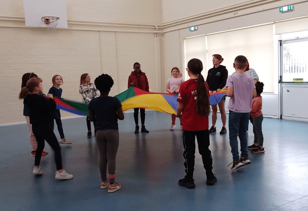 Young people attend a youth club event and take part in an activity with a parachute
